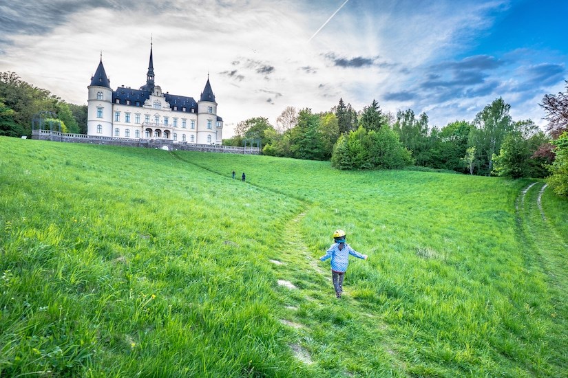 Ein Kind laeuft ueber die Wiese zum Schlosshotel Ralswiek